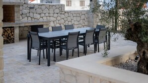 An outdoor patio with a stone wall, a wooden table with chairs, and a built-in grill. - Luxury Living at Horizon Retreat - Two Bedroom Apartment (Marina)