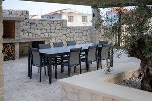 Eine Terrasse im Freien mit einer Steinsäule, einem Holztisch mit Stühlen und einem fest installierten Grill.