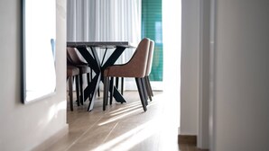 A dining area with a table and chairs, a window with curtains, and a view of a building outside. - Luxury Living at Horizon Retreat - Two Bedroom Apartment (Marina)