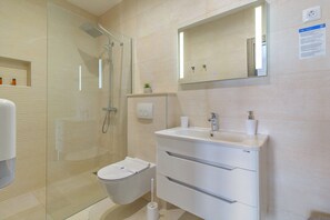Ein modernes Badezimmer mit Duschkabine aus Glas, Toilette, Waschbecken mit Spiegel und einer kleinen Ablage für Pflegeprodukte.