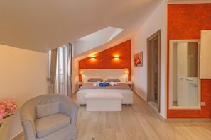 Ein Schlafzimmer mit einem Bett, Nachttischen, einer Bank, einem Sessel und einem Fenster.