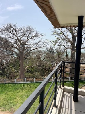 A balcony with a railing, a view of trees, and a grassy area.