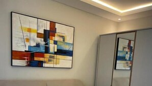 A hotel room with a bed, a large abstract painting, a mirror, and a wardrobe.