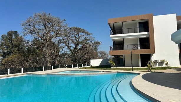 A modern building with a pool, surrounded by trees and a clear sky.