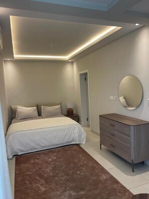 A bedroom with a bed, a dresser, a mirror, and a door. - Tanji Cliffs (Tanji)