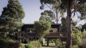 A modern two-story building with a wooden deck, surrounded by dense vegetation. - Stewie's Nest - Port Arthur Shack with fire pit (Tasman)