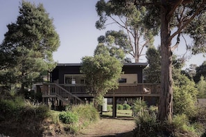 A modern two-story building with a wooden deck, surrounded by dense vegetation.