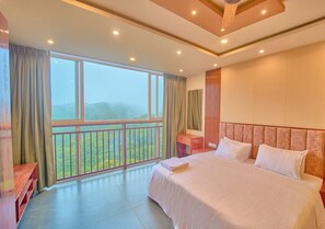 A bedroom with a large bed, a nightstand, a wooden bench, and a balcony with a view of greenery.