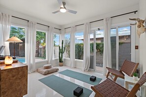 A spacious room with large windows, a ceiling fan, and a cactus plant. - Casa Serena Pool, Spa, Putting Green & Yoga Room (Tucson)