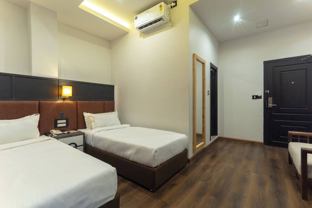 A hotel room with two beds, a bedside table with a phone, a wall-mounted air conditioner, and a door.