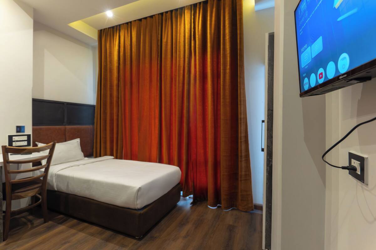 A hotel room with a bed, a desk, a chair, a television, and a curtain.