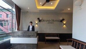 A hotel reception area with a marble reception desk, two wall-mounted light fixtures, a bench, and a sign reading 'Grand Hotel Annex'.
