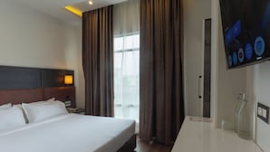 A hotel room with a bed, a nightstand, a TV, and a window with curtains. - GRAND HOTEL ANNEX (Aizawl)