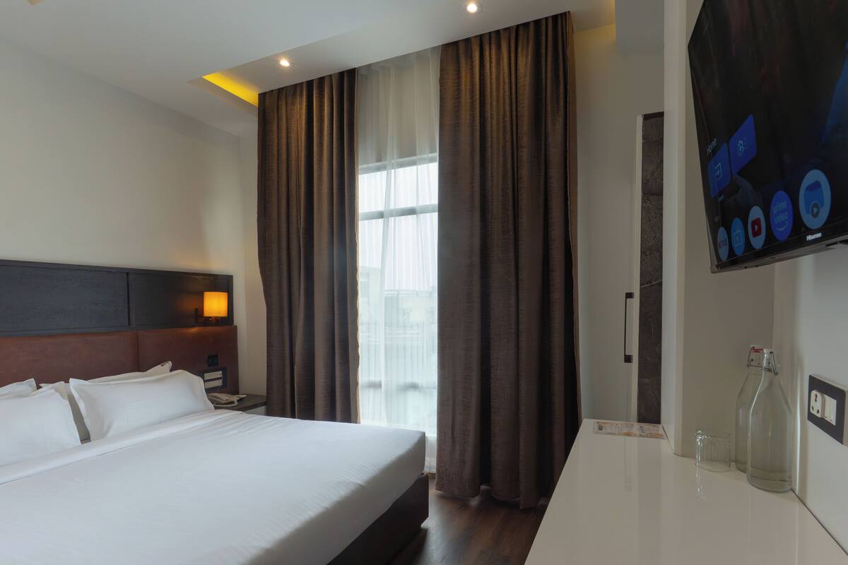 A hotel room with a bed, a nightstand, a TV, and a window with curtains.