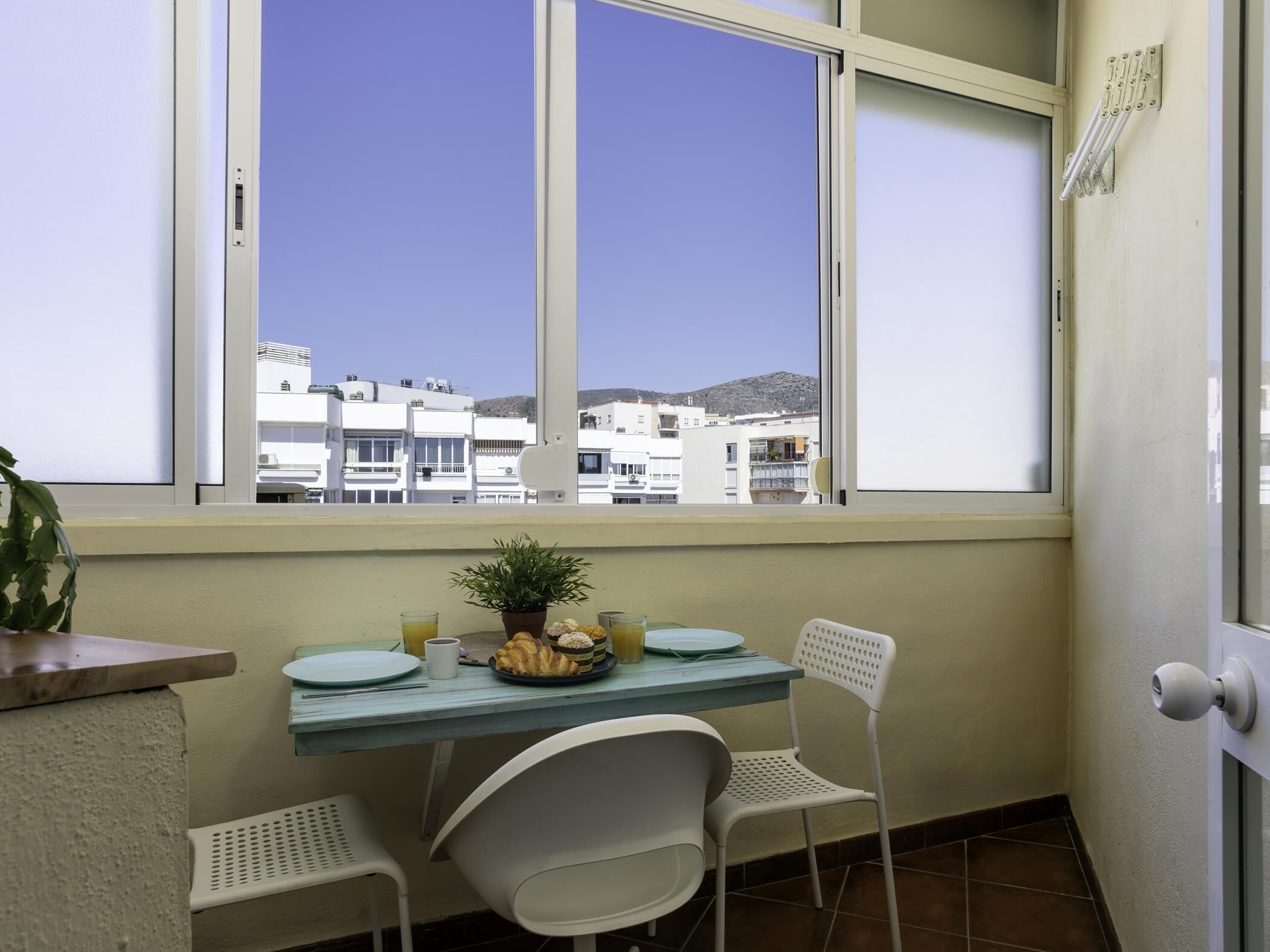 Un balcón con una mesa, sillas, una planta en maceta y vistas a edificios.