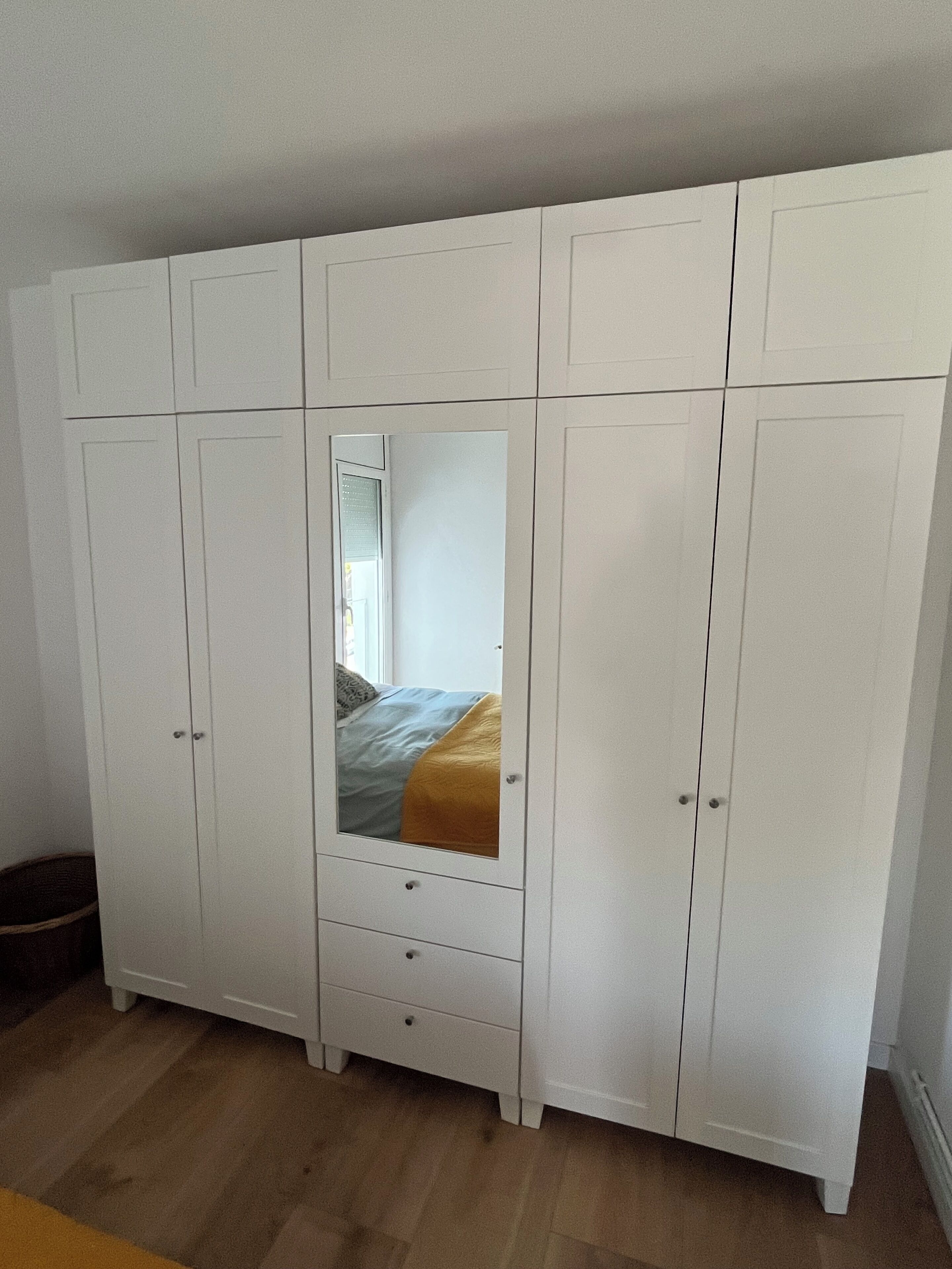 A white wardrobe with a mirror, drawers, and a bed with a blue and yellow bedspread.