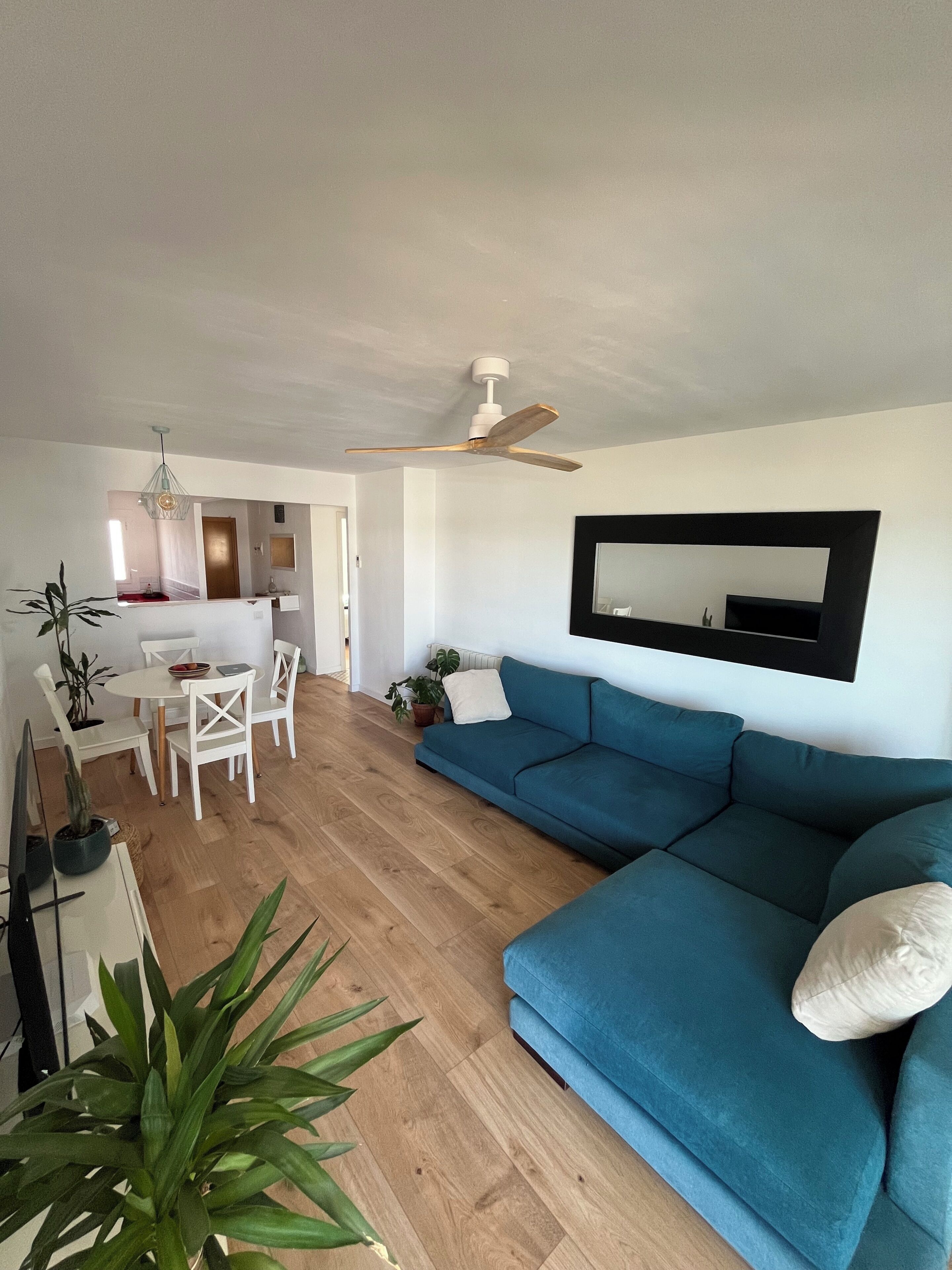 Un salon moderne avec un canapé bleu, un coin repas avec des chaises blanches et un ventilateur de plafond.