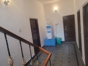 Un couloir avec un escalier, un distributeur d’eau, une poubelle et une porte.