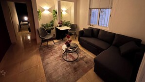 Ein Wohnzimmer mit einer Couch, Sesseln, einem Couchtisch, einem Esstisch und Topfpflanzen.