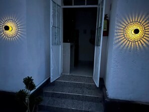 Eine Treppe führt zu einem dunklen Innenraum, begleitet von Wandleuchten mit Muster auf jeder Seite.