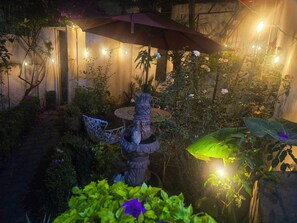 Ein Garten mit einem Steinfbrunnen, einem Tisch und Stühlen unter einem großen Sonnenschirm.
