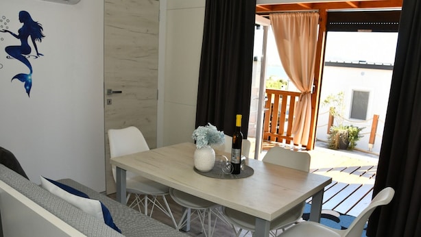 A dining area with a table, chairs, a bottle of wine, and a decorative vase. - Mobile Home With Terrace And Sea View (Pakostane)