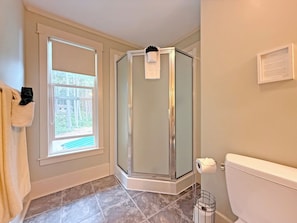 A bathroom with a glass shower enclosure, a toilet, a window with a view, and a towel rack.