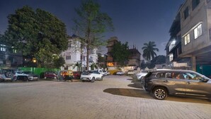 Un aparcamiento pavimentado con varios coches estacionados, rodeado de edificios y árboles.