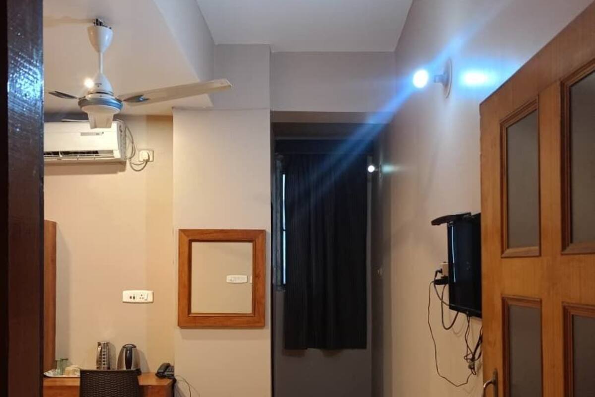 A hotel room with a bed, desk, chair, ceiling fan, and a television mounted on the wall.