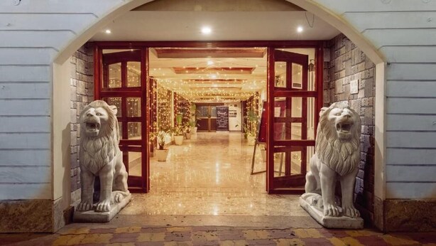 Una entrada arqueada con dos estatuas de leones, un pasillo con luces colgantes y un muro de ladrillo.