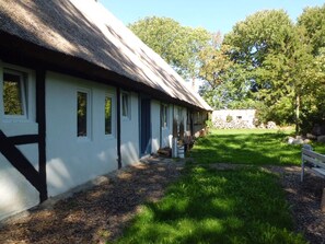 A traditional building with a thatched roof, a well-maintained lawn, and a stone wall in the background. - Charming 3-bedroom house in peaceful Dranske OT Gramtitz / island Ruegen (Dranske, OT Gramtitz)