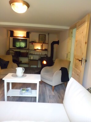 A cozy living room with a white sofa, a coffee table, and a television. There is a fireplace and a door to the right. - Charming 3-bedroom house in peaceful Dranske OT Gramtitz / island Ruegen (Dranske, OT Gramtitz)