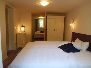 A bedroom with a large bed, a nightstand with a lamp, a wardrobe, and a window with curtains. - Charming 3-bedroom house in peaceful Dranske OT Gramtitz / island Ruegen (Dranske, OT Gramtitz)