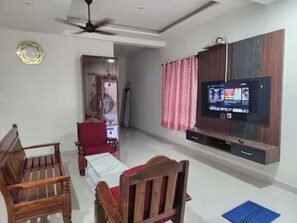 Ein Wohnzimmer mit Fernseher, Holzmöbeln und einem Deckenventilator.