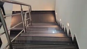 Eine moderne Treppe mit Metallgeländern und schwarzem Belag, die zu einem Raum mit großem Fenster und weißen Wänden führt.