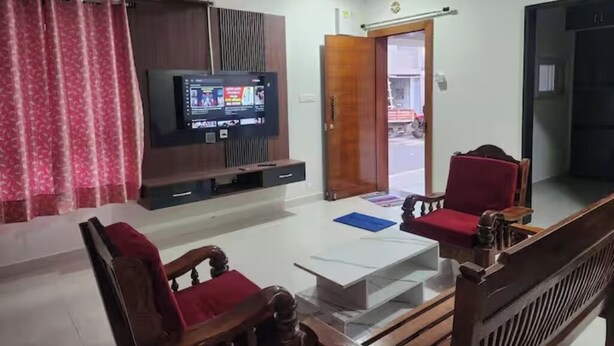 Ein Wohnzimmer mit Fernseher, einem Holzschrank, einem roten Sessel, einem weißen Couchtisch und einer Tür, die nach draußen führt.