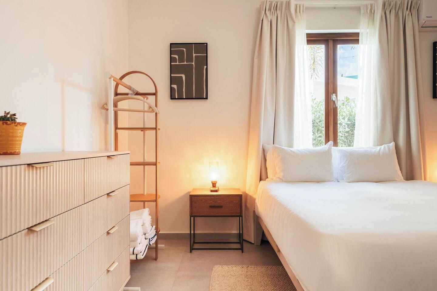 Un dormitorio con cama, mesita de noche, lámpara, armario y ventana con cortinas.