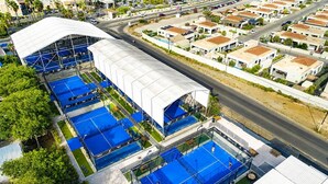 Un edificio grande con varias piscinas de techo azul, una zona cubierta y una calle con edificios residenciales.