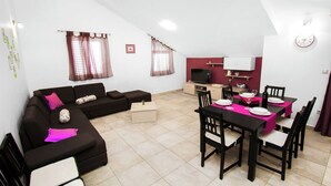 Un espacio habitable compacto con un sofá, una mesa de comedor lista para cuatro personas, un televisor y un reloj en la pared.
