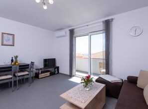 Ein modernes Wohnzimmer mit Sofa, Couchtisch, Fernseher und Essbereich mit Stühlen und Tisch.