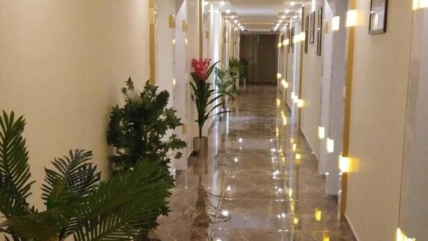 A hotel corridor with a marble floor, potted plants, and wall-mounted lights. - Hotel Royal King (Vadodara)