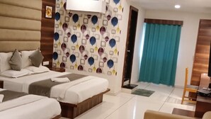 A hotel room with two beds, a sofa, a desk, and a patterned wall. - Hotel Royal King (Vadodara)