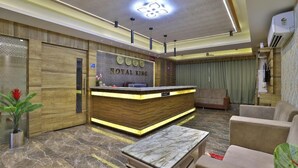 A reception desk with a wooden finish and 'ROYAL KING' signage, a marble-topped table, and a sofa in a modern lobby. - Hotel Royal King (Vadodara)