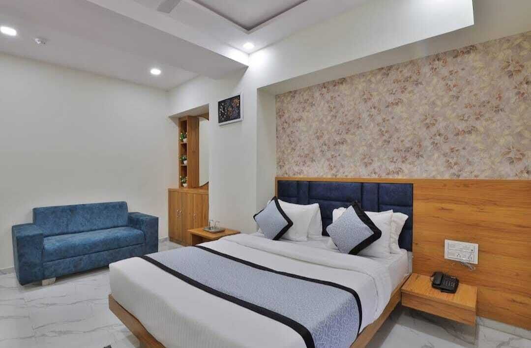 A bedroom with a bed, a blue sofa, a nightstand with a phone, and a wall with a floral pattern.