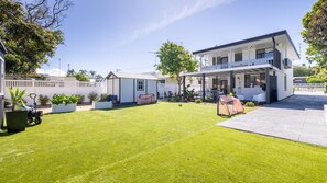 Ein modernes, zweistöckiges Haus mit gepflegtem Rasen, einer Terrassenfläche und einem kleinen Schuppen.