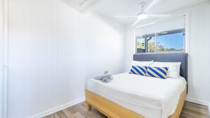 Ein Schlafzimmer mit Bett, Deckenventilator und Fenster mit Blick ins Freie.