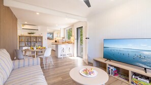 Ein modernes Wohnzimmer mit Sofa, Essbereich, Küche und einem Fernseher, der eine Strandansicht zeigt.