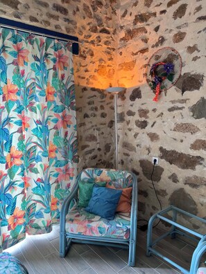 A room with a stone wall, a patterned curtain, a chair with cushions, and a floor lamp. - QUIET LOFT IN THE COUNTRYSIDE, 7 KM FROM AMENITIES (Saint-Bressou)