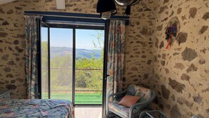 A room with a bed, a chair, and a view of a green landscape through a glass door. - QUIET LOFT IN THE COUNTRYSIDE, 7 KM FROM AMENITIES (Saint-Bressou)