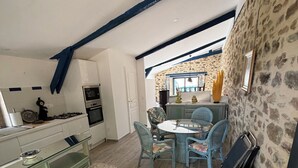 A kitchen with a gas stove, oven, and a dining area with a table and chairs. - QUIET LOFT IN THE COUNTRYSIDE, 7 KM FROM AMENITIES (Saint-Bressou)